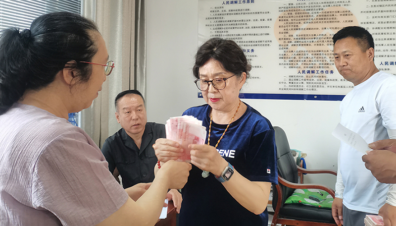 頭題片，5月30日,，某藥業(yè)公司按協(xié)議約定完成第一期履行義務(wù),，將十萬(wàn)現(xiàn)金交到法院，調(diào)解員付菊（左一）清點(diǎn)無(wú)誤之后交到農(nóng)民工委托代理人徐某手中